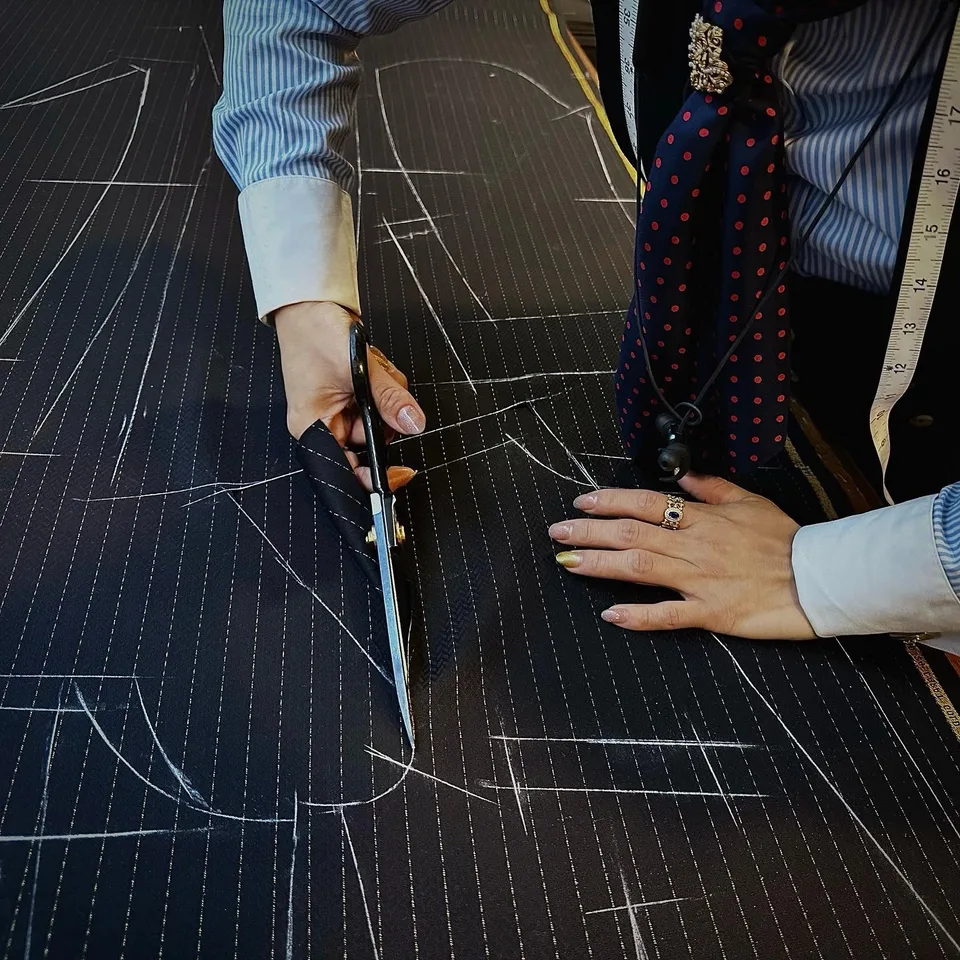 A cutter guides black shears through chalked navy pinstripe cloth at the worktable.