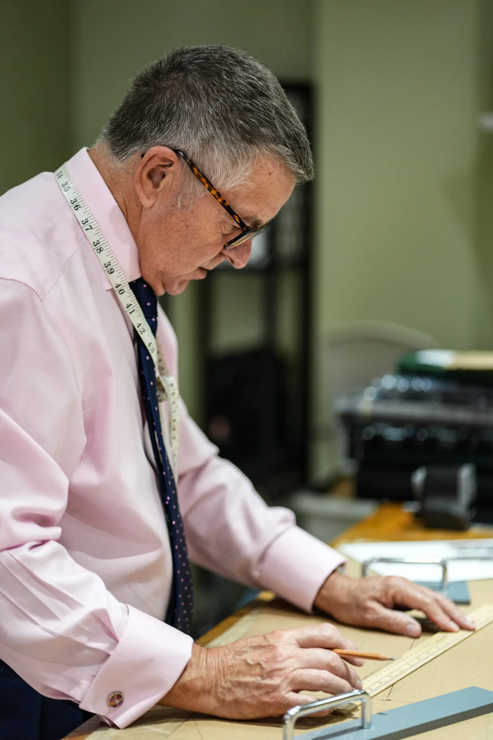 A master cutter drafts a bespoke pattern by hand at his worktable.