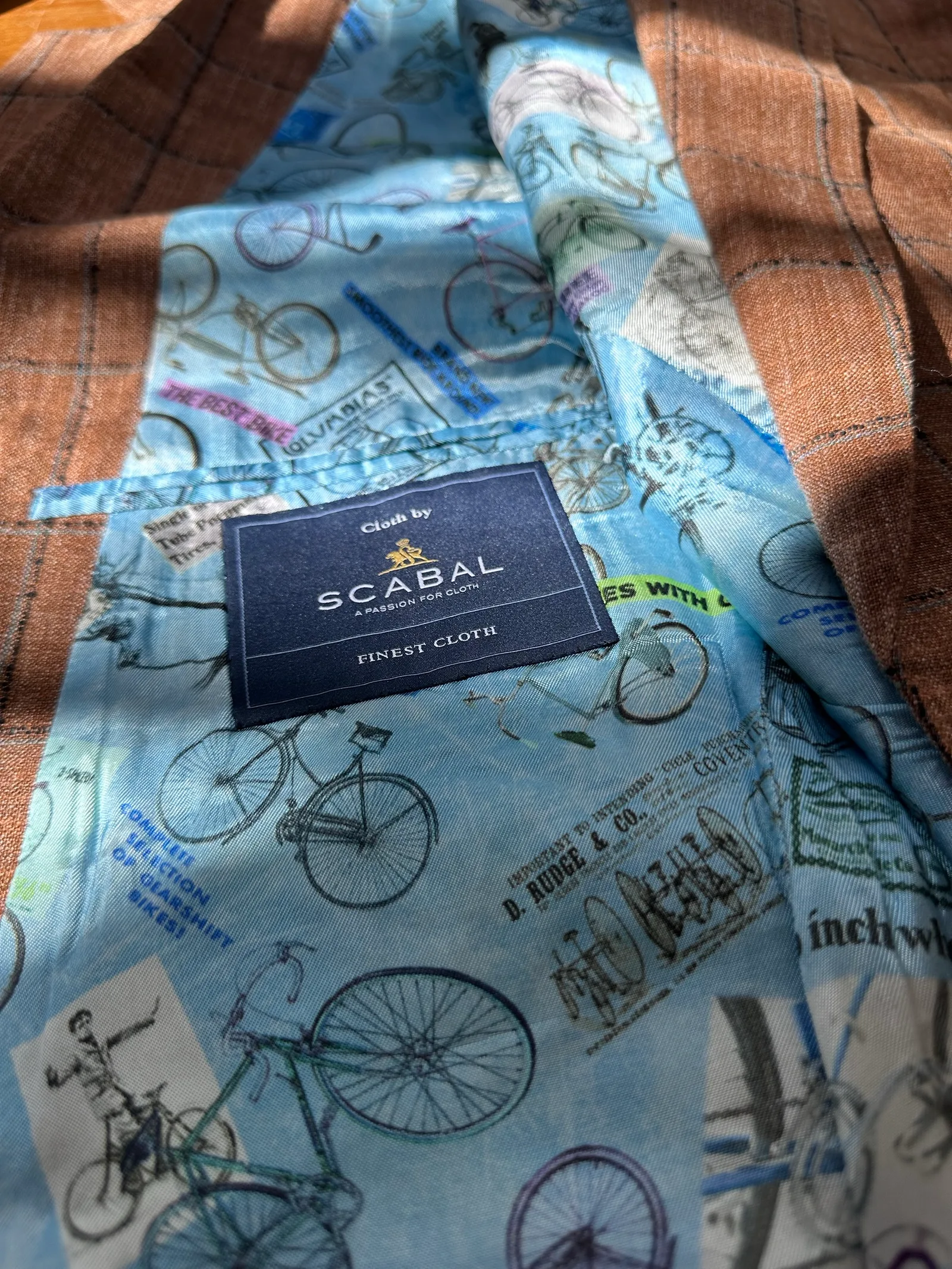 Interior view of a rust windowpane sport coat, revealing a pale-blue illustrated bicycle-and-map lining with Scabal label.