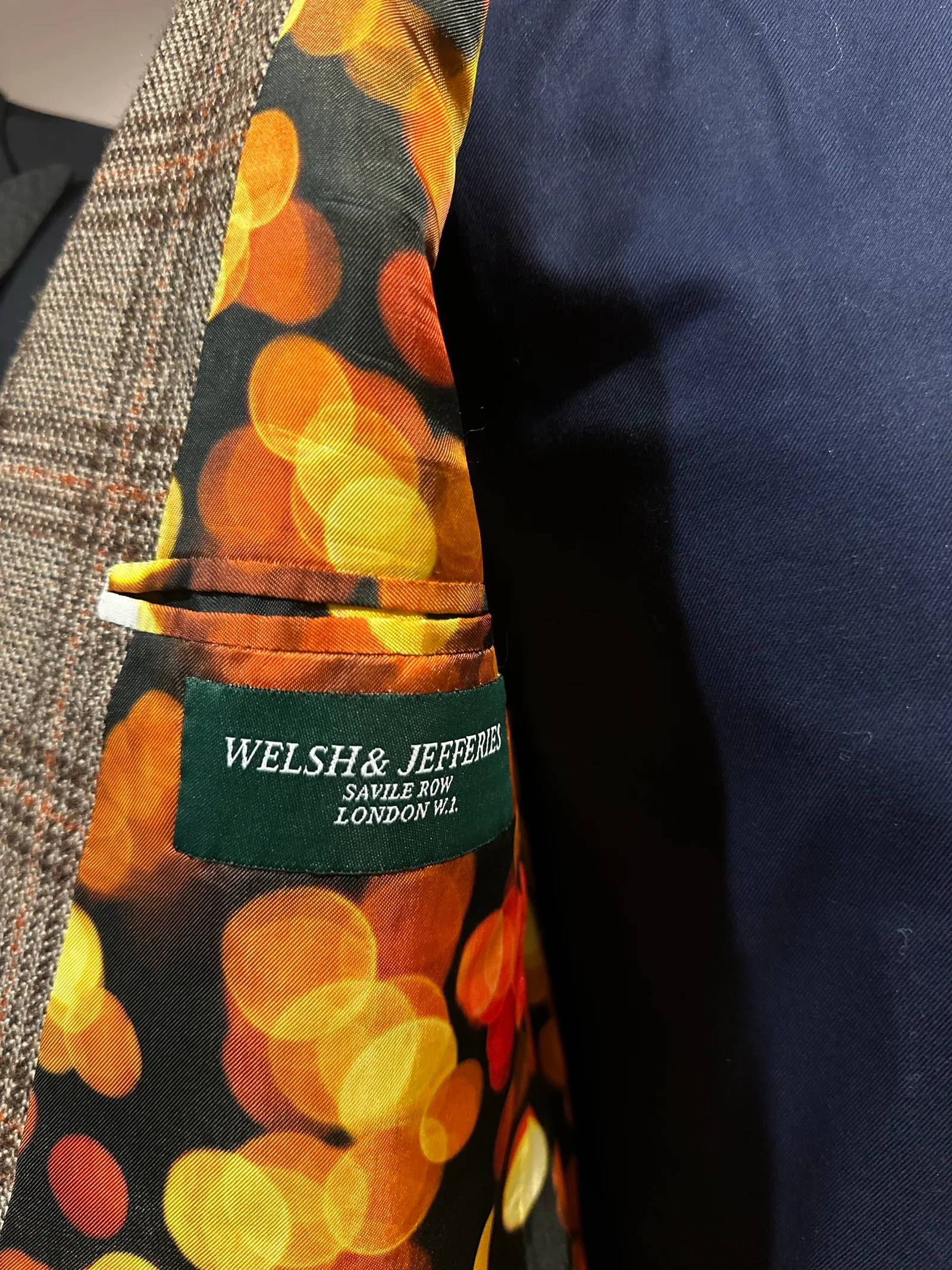Interior view of a brown Glen-check jacket with suede cuffs, revealing an orange bokeh-print lining and contrasting tan suede cuff facings.