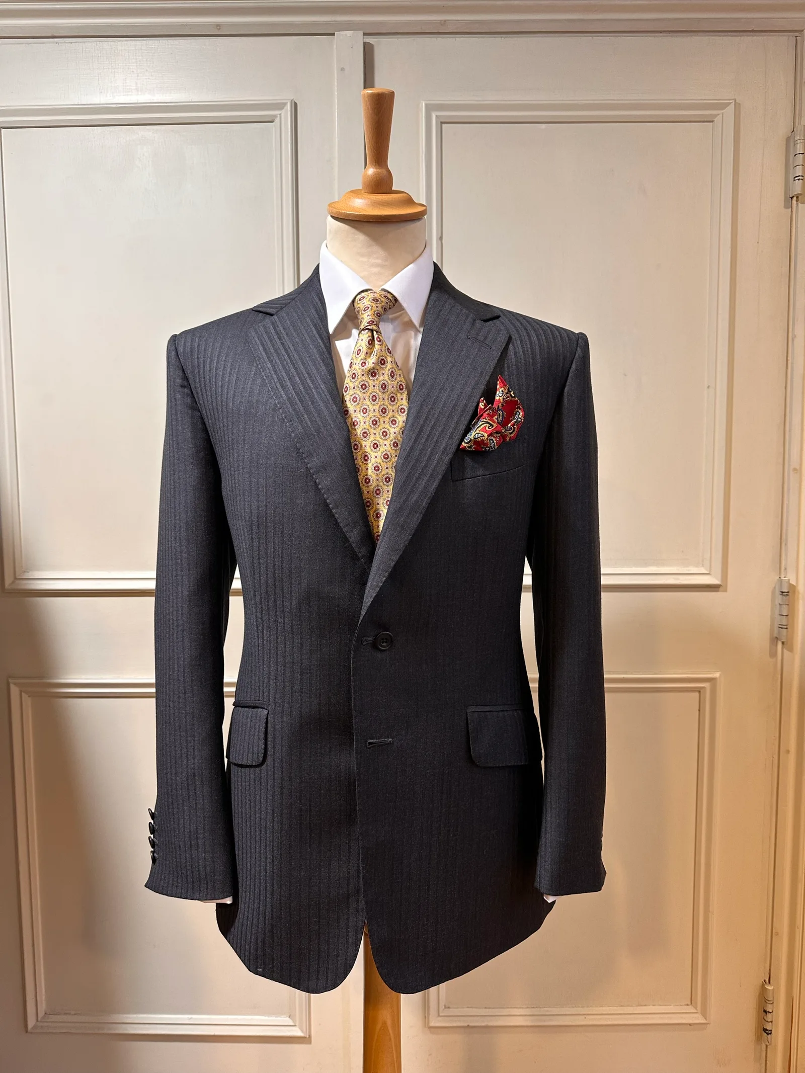 Front mannequin view of a charcoal shadow-stripe suit, showing tonal shadow stripes, notch lapels, flap pockets and black horn buttons.