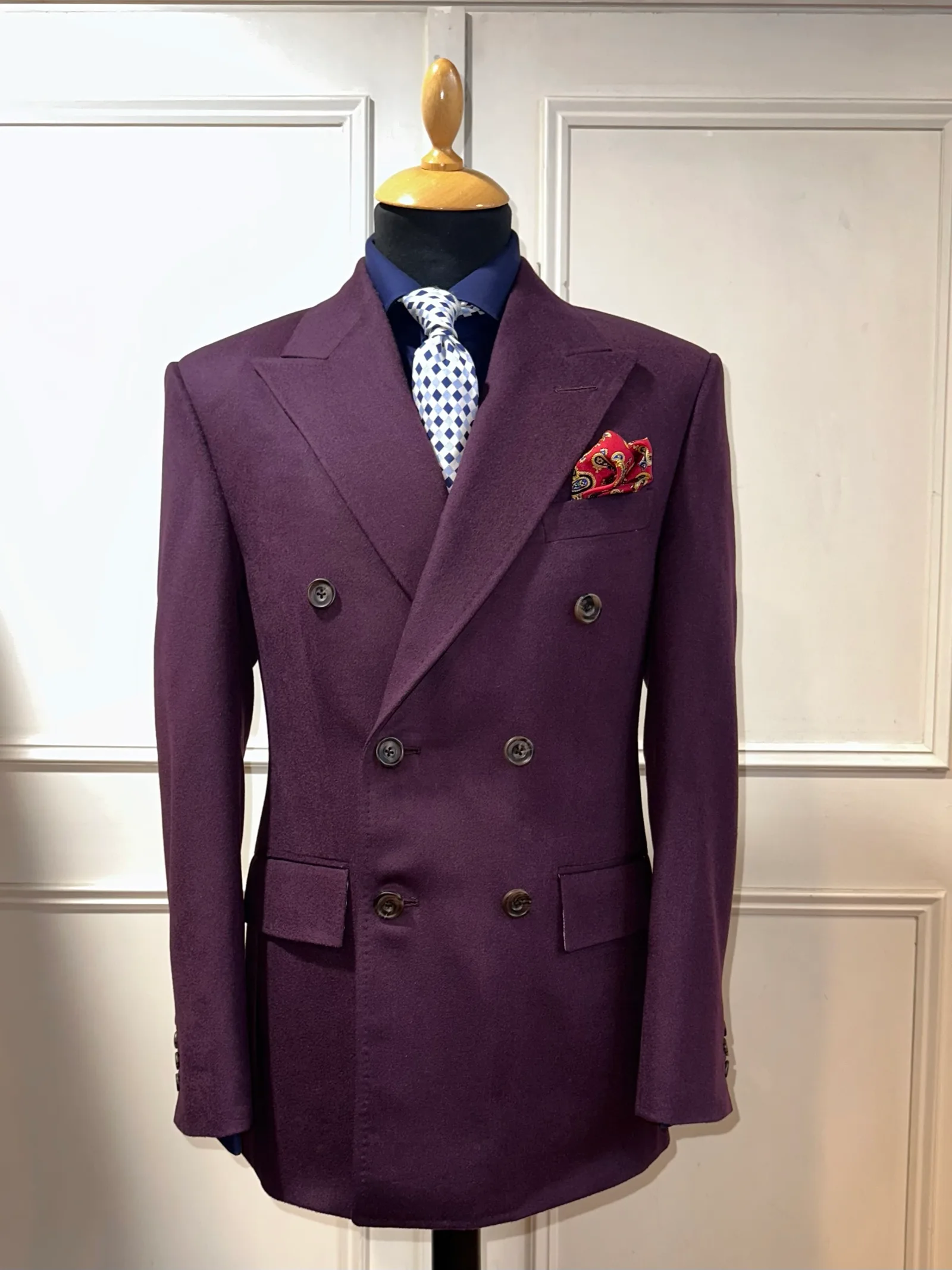 Front mannequin view of a deep mulberry double-breasted jacket, showing broad peak lapels, six dark horn buttons and a clean shaped waist.