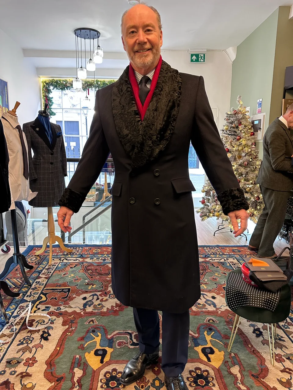 A smiling wearer models the long midnight cashmere coat with a deep black astrakhan-style collar.