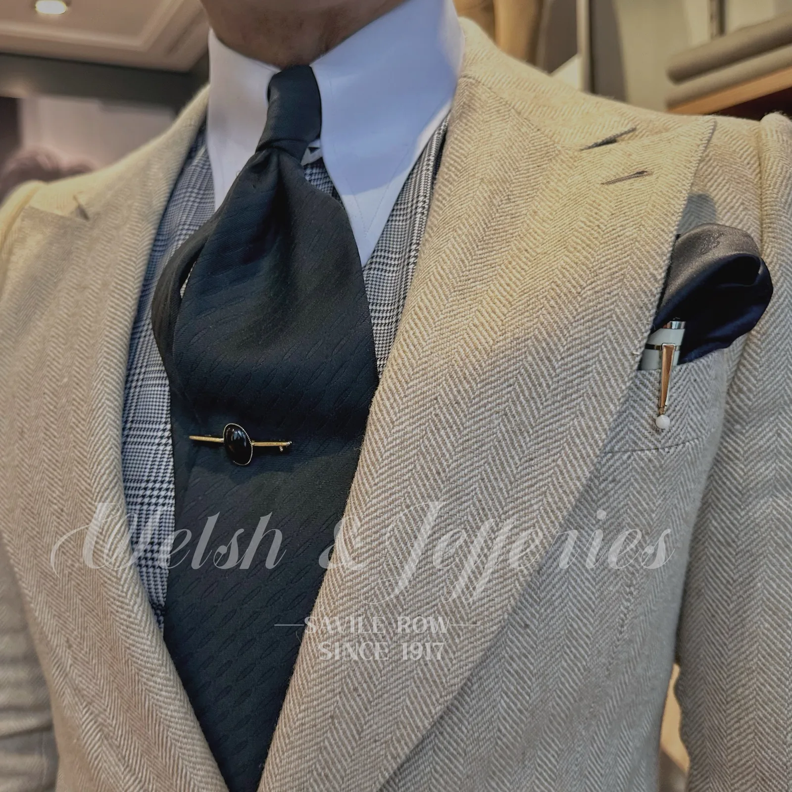 Restrained gold tie bar with a polished oval black onyx worn with a black tie and cream herringbone jacket.