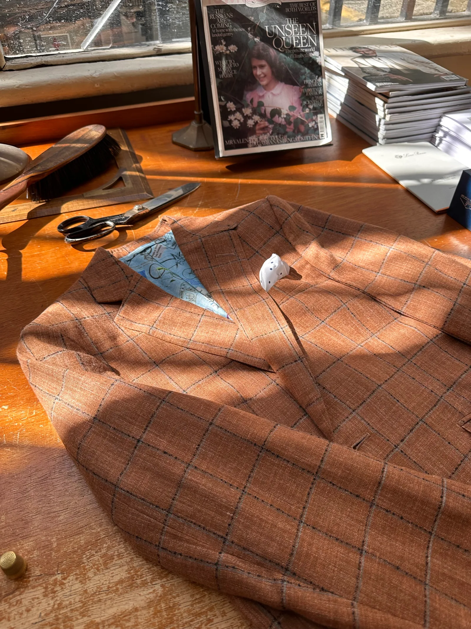 Worktable flat lay of a rust windowpane sport coat, showing navy windowpane, notch lapels, stacked hip pockets and pale horn buttons.