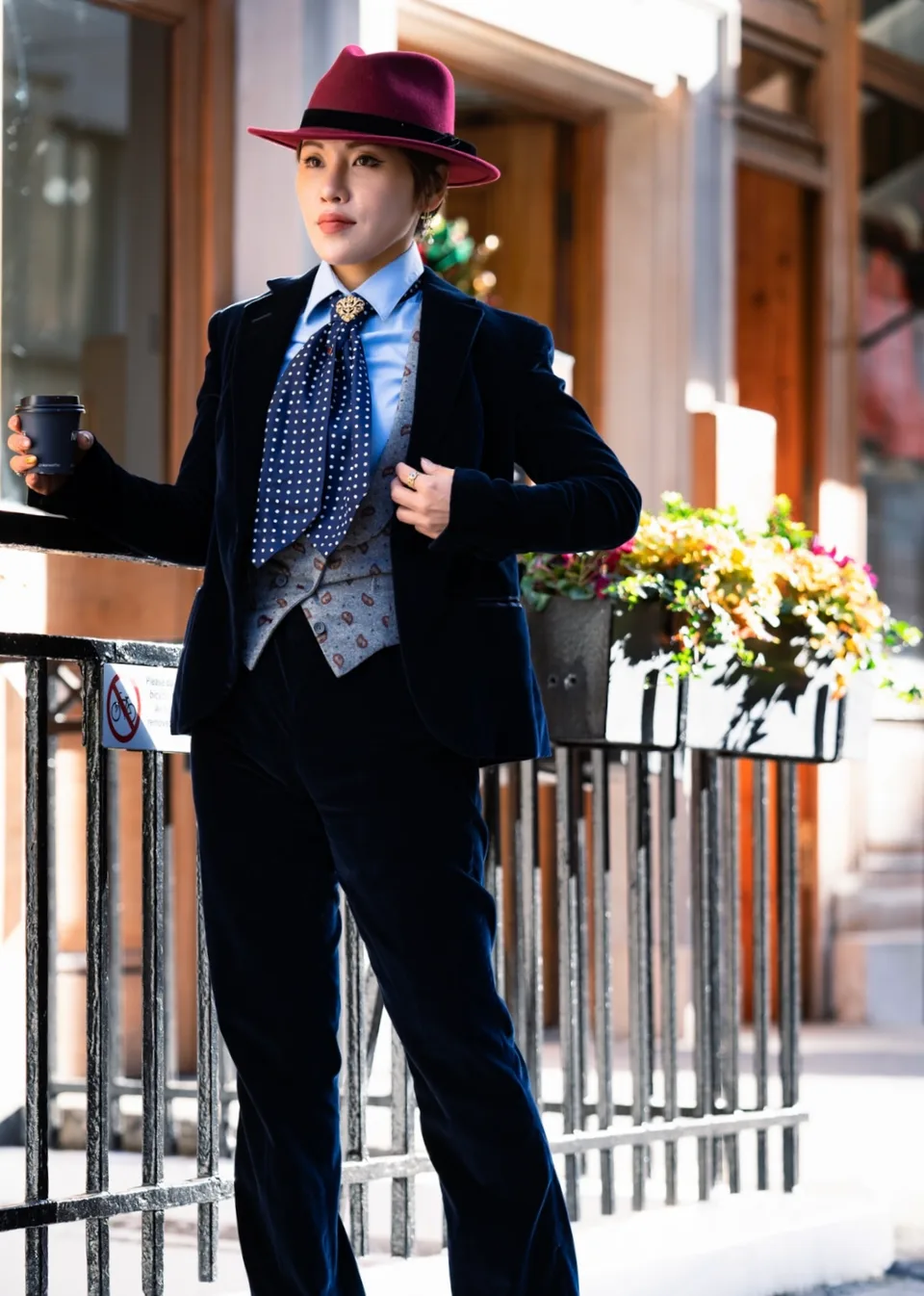 A woman in a navy velvet three-piece suit and burgundy hat.