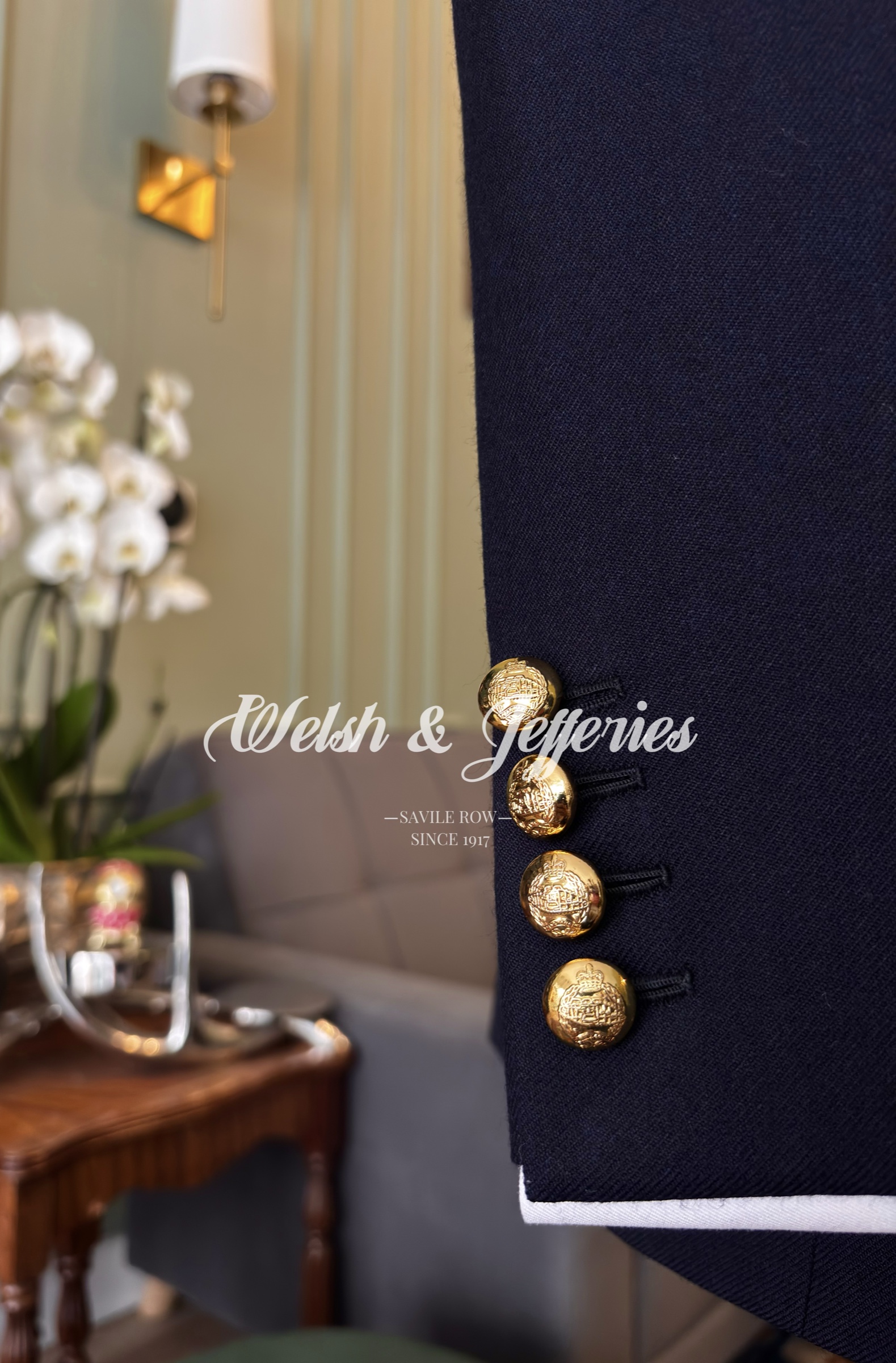 Close view of midnight barathea, gilt relief buttons and narrow white sleeve-edge piping.
