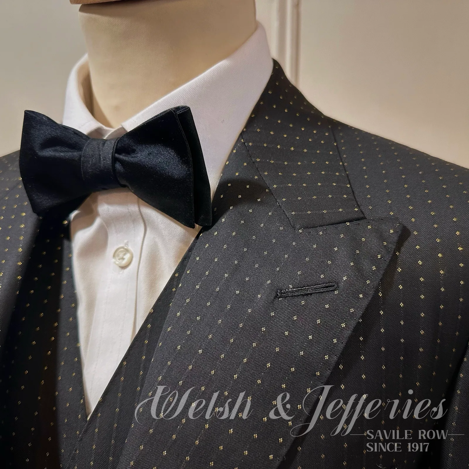 A peak lapel in midnight gold-dotted cloth frames a black bow tie and white shirt.