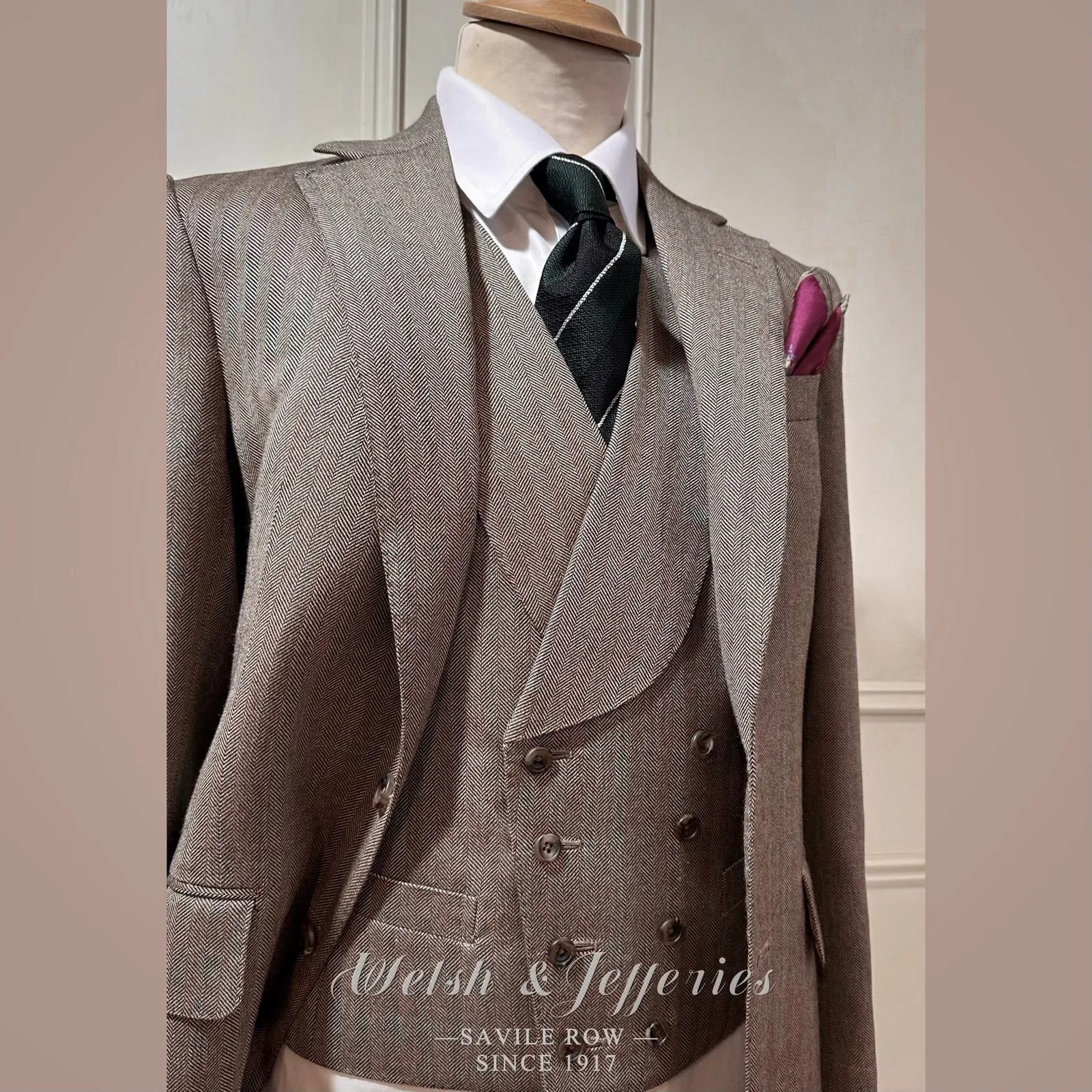 Taupe herringbone three-piece suit with a long clean front and matching waistcoat.