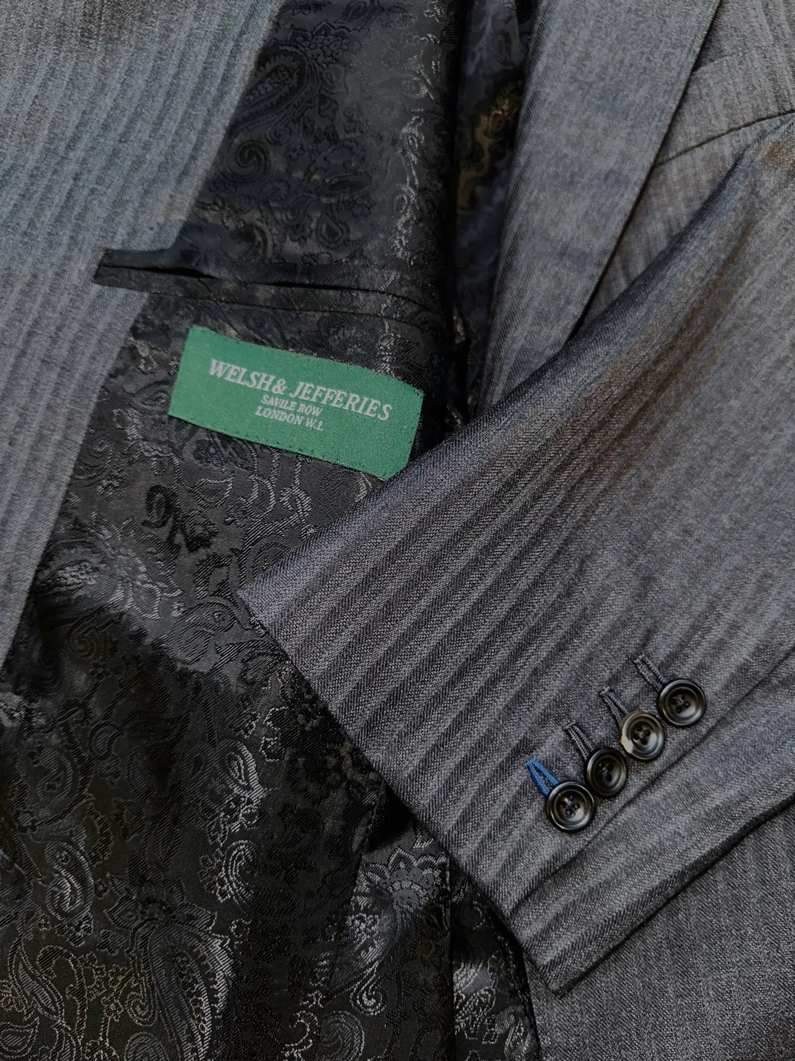 Interior view of a charcoal shadow-stripe suit, revealing black paisley-jacquard lining and four-button cuff finishing.