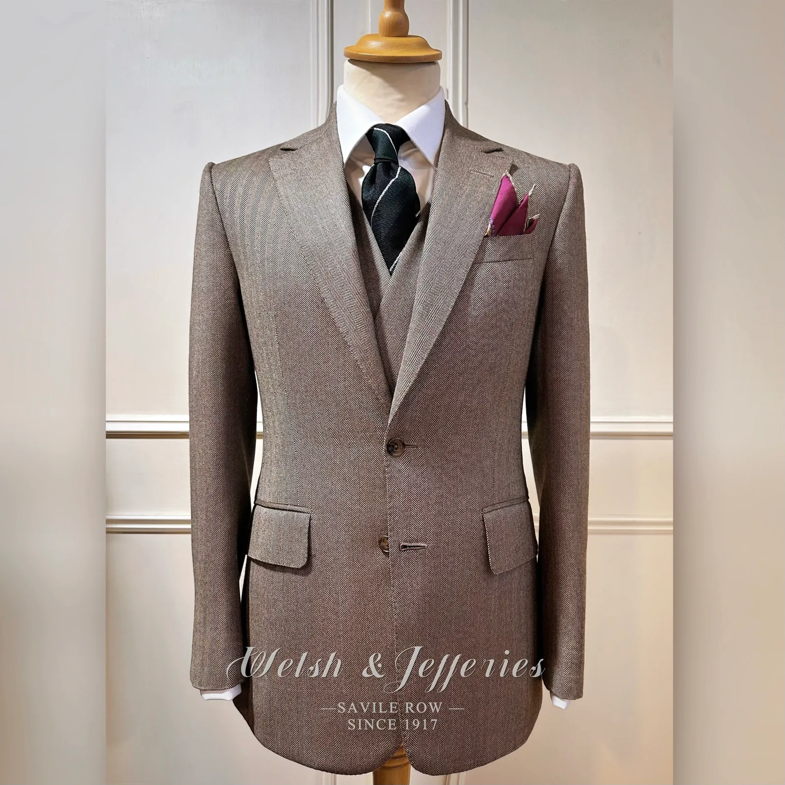Taupe herringbone three-piece suit with a long clean front and matching waistcoat.