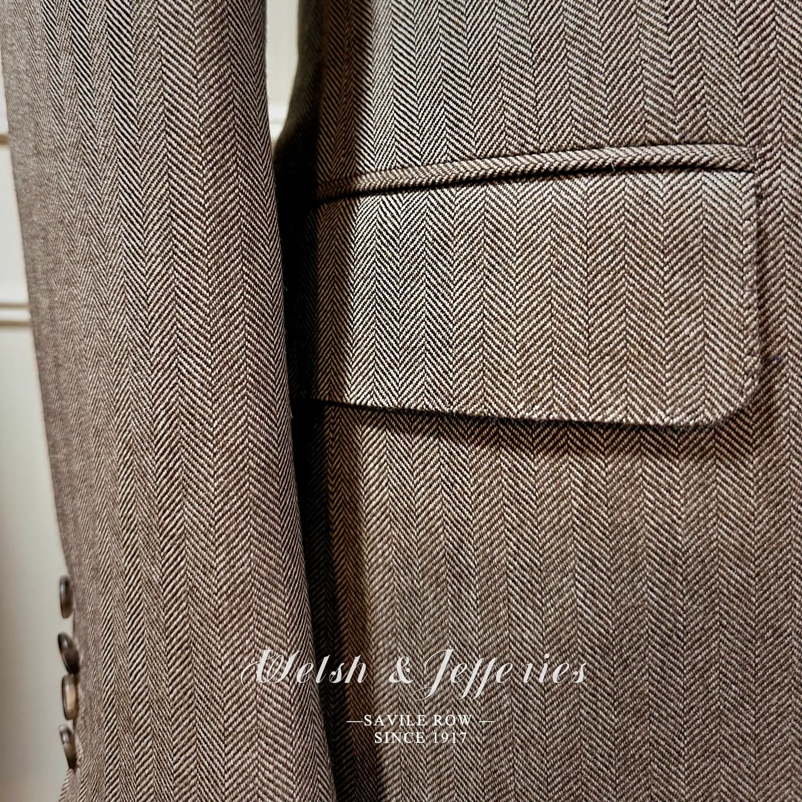 Close view of taupe herringbone, horn buttons, pocket finishing and map-print lining.