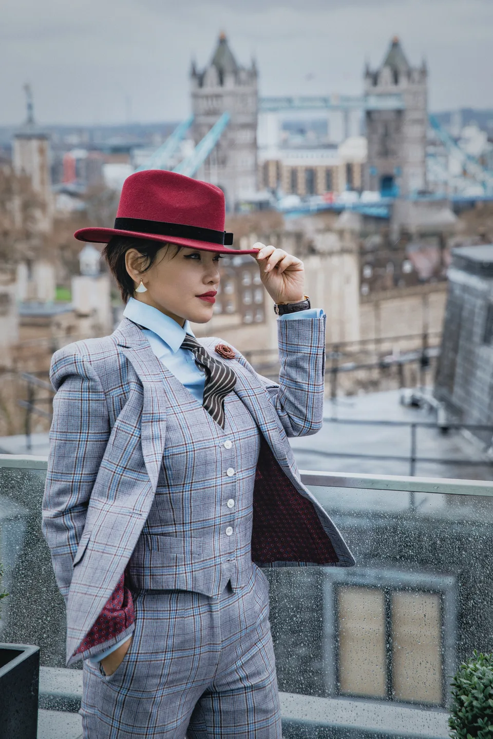 A woman in a grey checked three-piece suit and burgundy hat above London.