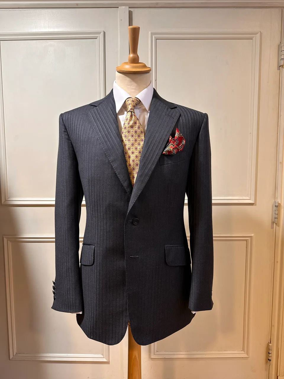 Front mannequin view of a charcoal shadow-stripe suit, showing tonal shadow stripes, notch lapels, flap pockets and black horn buttons.