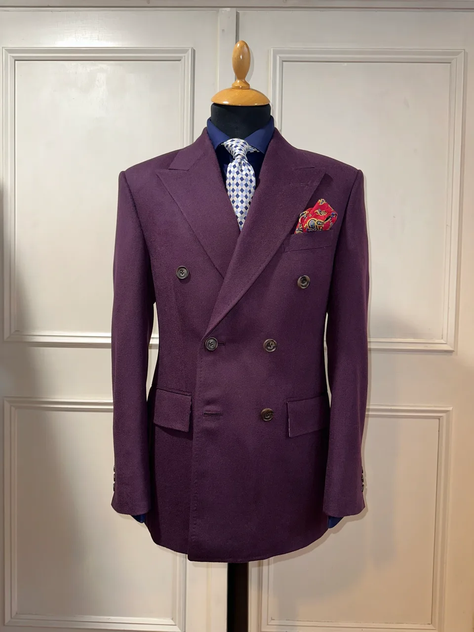 Front mannequin view of a deep mulberry double-breasted jacket, showing broad peak lapels, six dark horn buttons and a clean shaped waist.